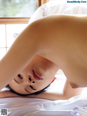 A naked woman sitting on a bed in front of a window.