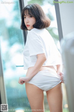 A woman in a white shirt and white panties leaning against a window.