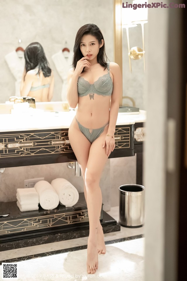 A woman in a gray lingerie standing in front of a mirror.