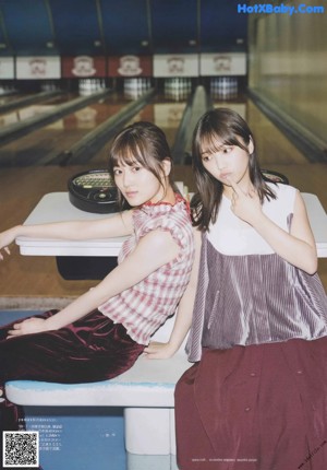 Two young women standing next to each other on scooters.