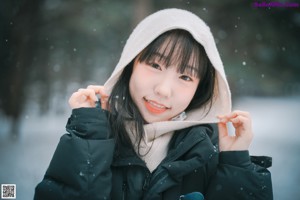 A woman in a black jacket and scarf standing in the snow.