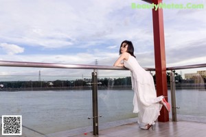 A woman in a black dress leaning against a wall.