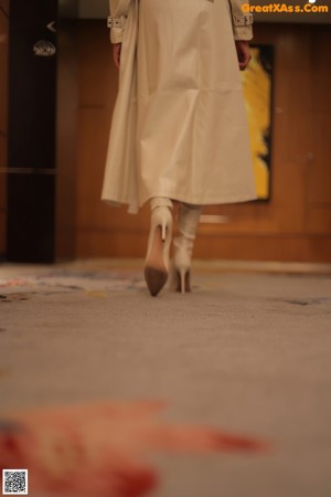 A woman in a beige trench coat is standing on a sidewalk.