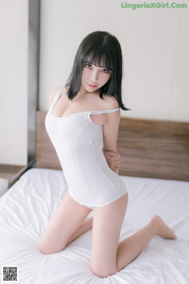 A woman in a white bodysuit sitting on a bed.