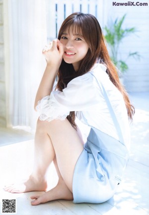 A woman in a blue dress leaning against a wooden wall.