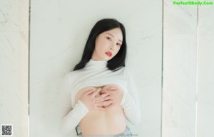 A woman sitting on top of a bed in a white shirt and skirt.