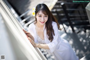 A woman in a white robe leaning against a wall.