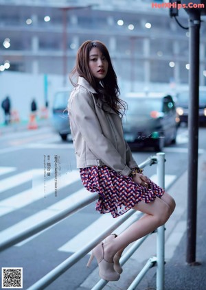 A woman sitting on a railing in the middle of a city.