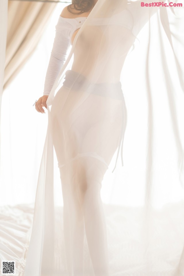 A woman in a sheer white dress standing on a bed.