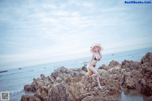 A woman in a bikini standing on a rocky beach.