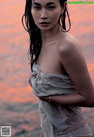 A woman in a white dress leaning against a wall.