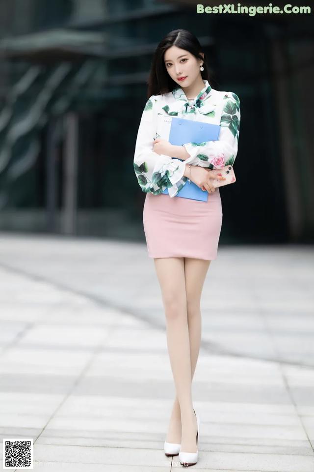 A woman in a white shirt and pink skirt holding a blue folder.