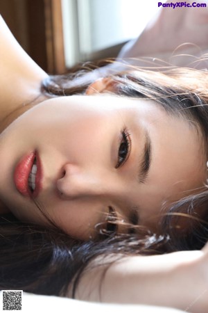 A naked asian woman standing in front of a window.